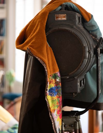 Parka Frida en tissu recyclé, posée sur un projecteur, avec doublure asymétrique en laine et capuche doublée en polaire, illustrant son style unique.