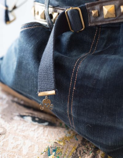 Zoom sur le Sac Rock en denim recyclé, avec une anse en ceinture cloutée et des poches fonctionnelles intégrées.